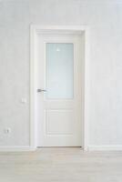 In an empty room, there stands a white door that features a glass window, adding a bit of natural light to the otherwise vacant space, enhancing the overall aesthetic of the area photo
