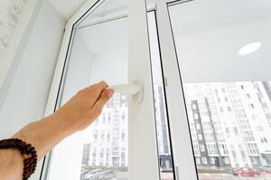 Man opens window to the street, white handle of plastic window. photo