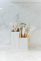 A white container that is filled to the brim with various kitchen utensils sitting prominently on a kitchen counter, ready for use and adding a splash of organization to the space photo