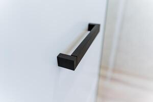 This closeup image showcases a stylish black handle against a white wall, highlighting its innovative design and intricate texture that captivates the viewers attention photo
