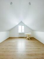 In the spacious and empty attic, there exists a simple yet functional table accompanied by several chairs, creating an inviting space for various activities and gatherings photo