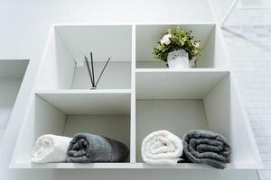 A white shelf with towels and a vase of flowers on it photo