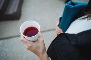 A woman is holding a cup filled with a red beverage while surrounded by various documents and paperwork photo