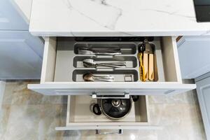 Inside a kitchen drawer, one can find a variety of utensils, pots, and pans, all carefully arranged and filled, ready to be used for various cooking and food preparation tasks photo