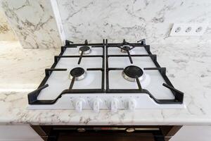 This elegant and modern kitchen showcases a sleek gas cooktop equipped with four efficient burners, perfectly set against a stylish marble countertop photo