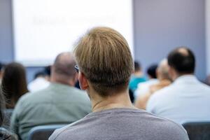 A man is currently sitting in a classroom environment attentively watching a presentation being delivered by someone, possibly as part of an educational training session photo