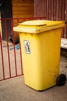 This is a bright yellow trash bin on wheels placed strategically in an urban setting for easy access and use photo