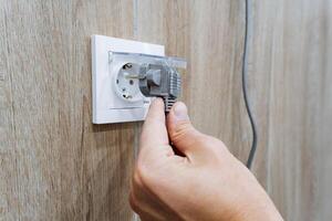 A person is carefully inserting a plug into an electrical outlet, which is a common and essential task required to supply power to various devices for their optimal usage and performance photo