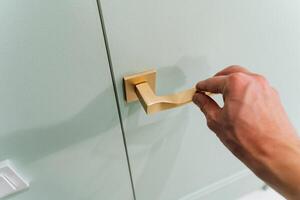 A person is elegantly opening a door that boasts a beautifully designed gold handle, which is often associated with household hardware and improved security features for added safety photo