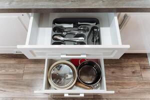 A kitchen drawer that is filled to the brim with various pots, pans, and an assortment of silverware, creating a useful and organized cooking space for culinary activities photo