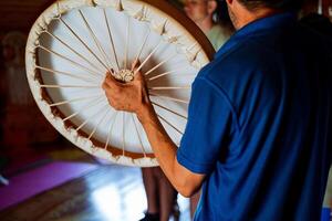 A man wearing a vibrant blue shirt is confidently holding a drum in both of his hands, showcasing his artistic talent and connection to the world of music and performance photo