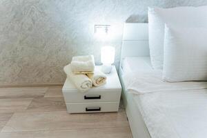 The space is a cozy bedroom that features a comfortable bed and a nightstand. On the nightstand, you can find some neatly arranged towels, adding to the rooms functionality and style photo