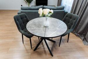 In a cozy living room, there is a round dining table accompanied by four comfortable chairs, and elegantly placed on the table is a beautiful vase filled with colorful flowers photo