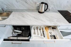 The kitchen is equipped with a sleek, modern dishwasher along with a spacious drawer filled with an array of utensils, making it perfect for all your meal preparation and cooking needs photo