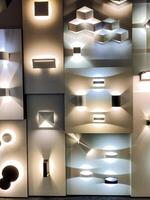There is a wall that showcases a wide variety of distinct types of lighting fixtures creatively arranged upon it, creating an interesting visual display of light and design photo