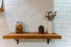 There is a beautifully crafted wooden shelf that features a delightful jar filled with freshly baked cookies, as well as a lovely vase overflowing with vibrant flowers that sit atop it photo