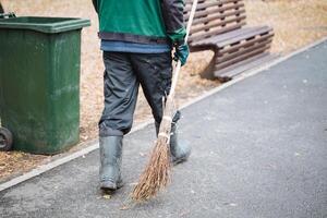 A man is casually strolling down a meticulously maintained sidewalk, gripping a broom firmly in his hand, prepared to clean up any debris or litter that may have accumulated along his path photo