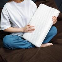 A woman comfortably relaxes on a plush, cozy couch, resting a fluffy white pillow gently on her lap while savoring a welldeserved moment of leisure amidst a calm and serene atmosphere photo