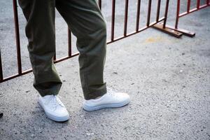 There is an individual who is dressed in white shoes and is currently positioned in front of a wooden fence, creating a visible contrast against the background of asphalt photo