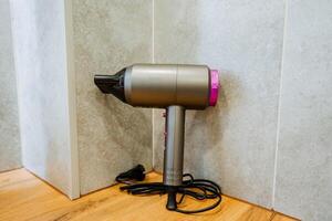 A hair dryer is currently placed on a beautiful wooden floor, which is situated directly next to a sturdy wall, creating a cozy and functional space for personal grooming activities photo