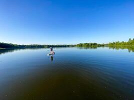 A serene scene unfolds as a person peacefully paddles on a tranquil lake, surrounded by natures beauty under a clear sky, creating a calm and peaceful atmosphere in this tranquil setting photo