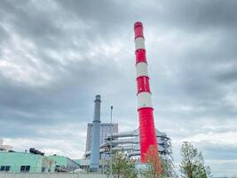 A factory that boasts a striking red and white chimney prominently stands out against a moody, cloudy sky, creating a dramatic urban landscape that unmistakably captures attention photo