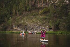 A confident person skillfully balances on a paddle board in the serene and calm waters, taking in the beauty of a lovely day that is filled with lush greenery and vibrant flowers all around photo