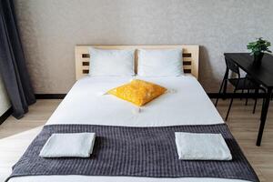 In a cozy bedroom, there is a beautifully arranged bed adorned with a vibrant yellow pillow, adding a cheerful touch to the overall decor of the room, making it feel inviting and warm photo