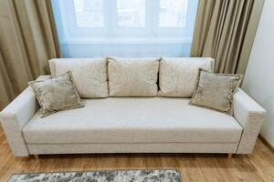 A plush, white couch is elegantly positioned in a cozy living room next to a beautifully framed window, allowing natural light to fill the space, enhancing the inviting atmosphere photo