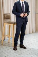 A welldressed man wearing a formal suit and a stylish tie is standing beside a chair, presenting an elegant and polished appearance that is appropriate for various formal occasions photo