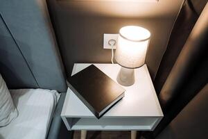 On the nightstand, a book is comfortably resting, placed adjacent to a lamp that casts a warm, gentle glow over the surrounding area, creating a cozy atmosphere for reading and relaxation photo