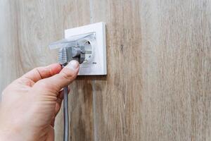 A person is carefully plugging a cord into an outlet, which is a common and routine action in modern households as they connect various devices to power sources for functionality photo