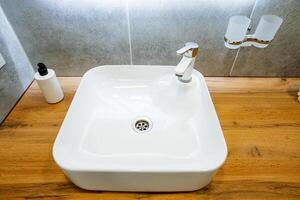 In the bathroom, there is a white sink gracefully positioned on a beautiful wooden counter, adding elegance to the overall ambiance of the space. It serves as a practical plumbing fixture photo