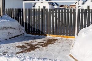 The adjoining territory, the entrance to the house is cleared of snow, the gate is made of corrugated sheeting, the fence is picket. Winter in the yard. photo