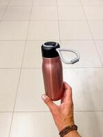 The detailed photograph captures a person holding a pink water bottle, emphasizing their hand movements and the bottles design, suggesting they are preparing to drink from it photo