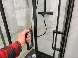 A person is currently engaged in the process of opening a bathroom shower door, which suggests that they are likely getting ready to take a shower or clean themselves up in that space photo