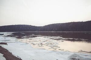 A Lake With Mountains In The Background And Ice On The Shore photo