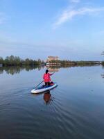 A person is paddleboarding on a calm lake under a clear sky, enjoying the peaceful atmosphere in nature photo