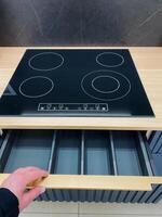 A person is in the kitchen, actively opening a drawer located next to the stove top, which is a major appliance used for cooking and food preparation in a home environment photo