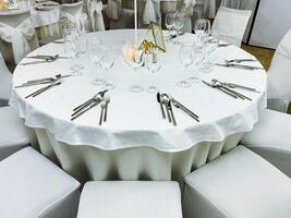 A beautifully arranged round table featuring pristine white linens and polished silverware is perfectly set up and ready for a delightful wedding reception event to gracefully unfold photo