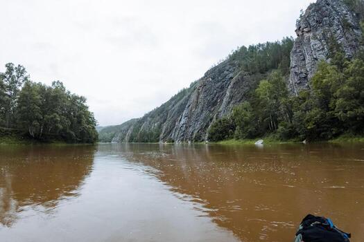 The tranquil image captures a person in a boat, floating on a river encircled by majestic mountains, forming a stunning setting with water, sky, trees, and other elements of nature photo