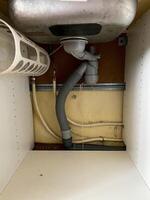 The image displays the underside of a kitchen sink with a hose connected, likely a plumbing fixture. Keywords include composite material, plumbing fitting, pipe, and metal photo