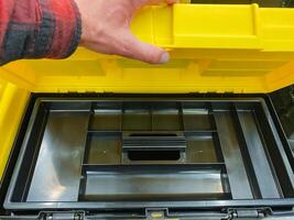 A person is currently in the process of opening a vibrant and bright yellow plastic toolbox that likely holds various tools intended for repair, maintenance, or construction tasks photo