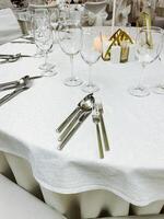 A beautifully arranged white table cloth which is elegantly set with silverware and sparkling wine glasses placed gracefully on top of it, creating an inviting dining atmosphere photo