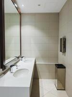 This welldesigned bathroom features a spacious layout with two sinks, a large mirror for grooming, and a strategically placed trash can for cleanliness and organization photo