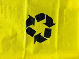The item in question is a vibrant yellow bag that features a bold black recycling symbol prominently displayed upon its surface, indicating its environmental significance photo