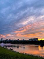 A stunning sunset gracefully casts its colors over a serene lake, while a vibrant city skyline stands majestically in the background, creating a picturesque blend of nature and urban life photo