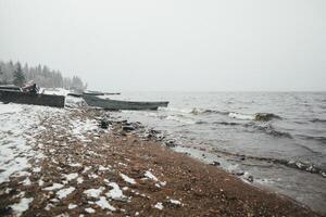 A Snowy Beach With Boats In The Water And Trees In The Background photo