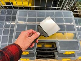 A hand is firmly grasping a putty knife positioned just above a storage container that features neatly organized compartments inside it photo