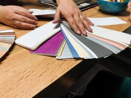 A womans hands are skillfully reaching out for a colorful swatch of fabric that is placed on a surface of a table, indicating her attention to detail and design choices photo